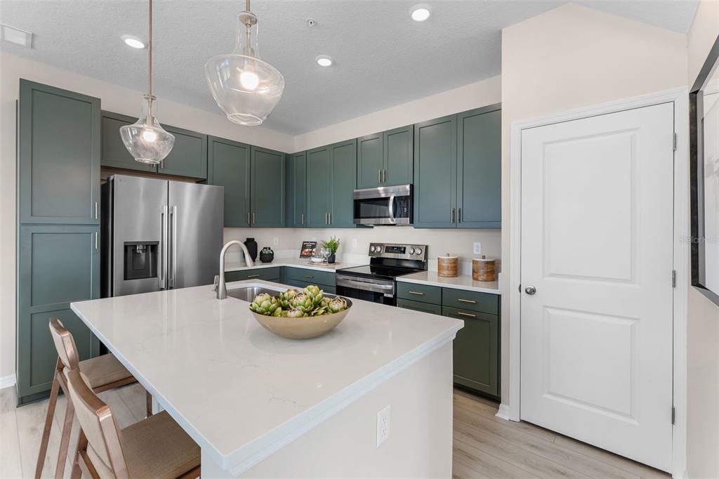 A kitchen features green cabinets, a white quartz island, and stainless steel appliances — 722 BLISSFUL GARDENS WAY, APOPKA, FL