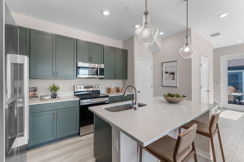 A modern kitchen features sage green cabinets, a quartz-topped island, and stainless steel appliances — 722 BLISSFUL GARDENS WAY, APOPKA, FL