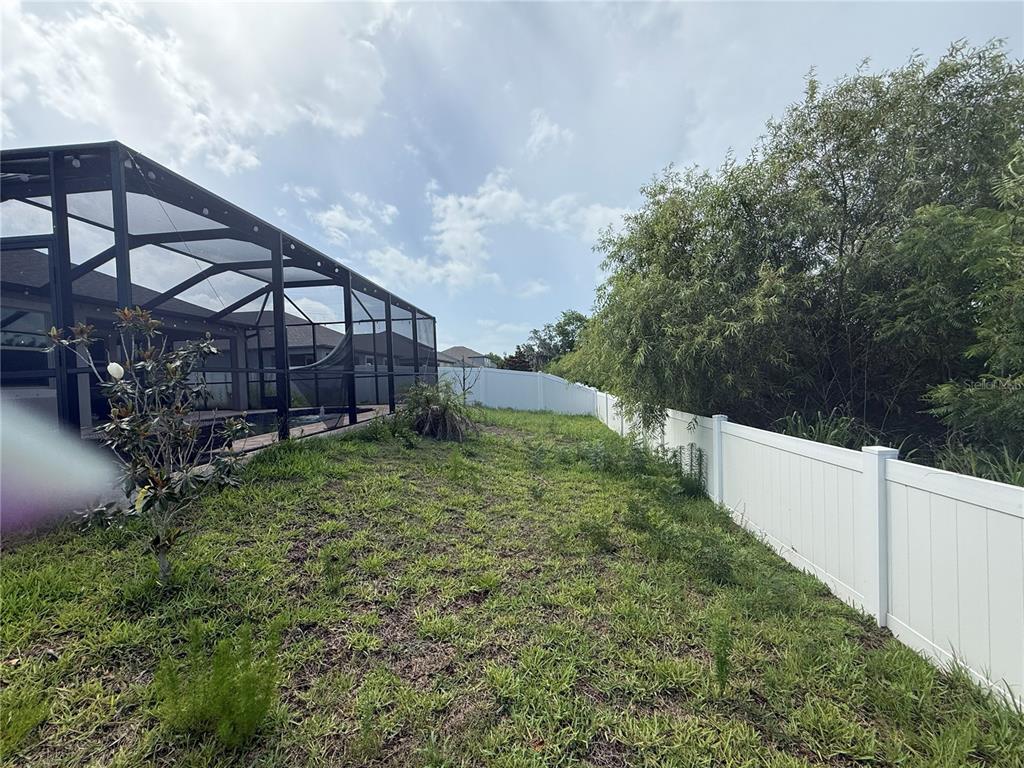 A backyard features a screened-in pool enclosure, a white vinyl fence, and grassy landscaping — 11865 SUNBURST MARBLE ROAD, RIVERVIEW, FL