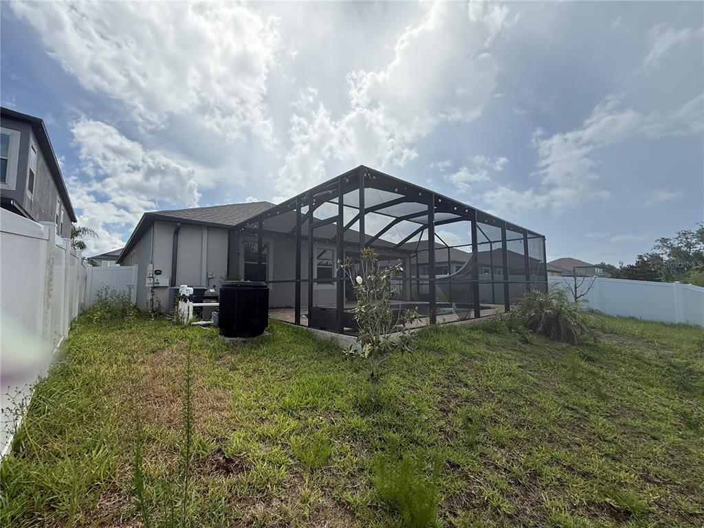 A backyard view of a house with a screened-in pool enclosure and a white fence — 11865 SUNBURST MARBLE ROAD, RIVERVIEW, FL