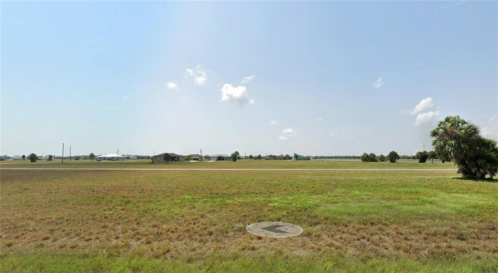 A wide, grassy vacant lot under a clear blue sky with distant houses visible — 7 SUNFLOWER LANE, PLACIDA, FL