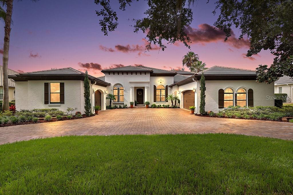 A single-story white stucco house with a paver driveway and a three-car garage at dusk — 9620 SAN FERNANDO COURT, HOWEY IN THE HILLS, FL