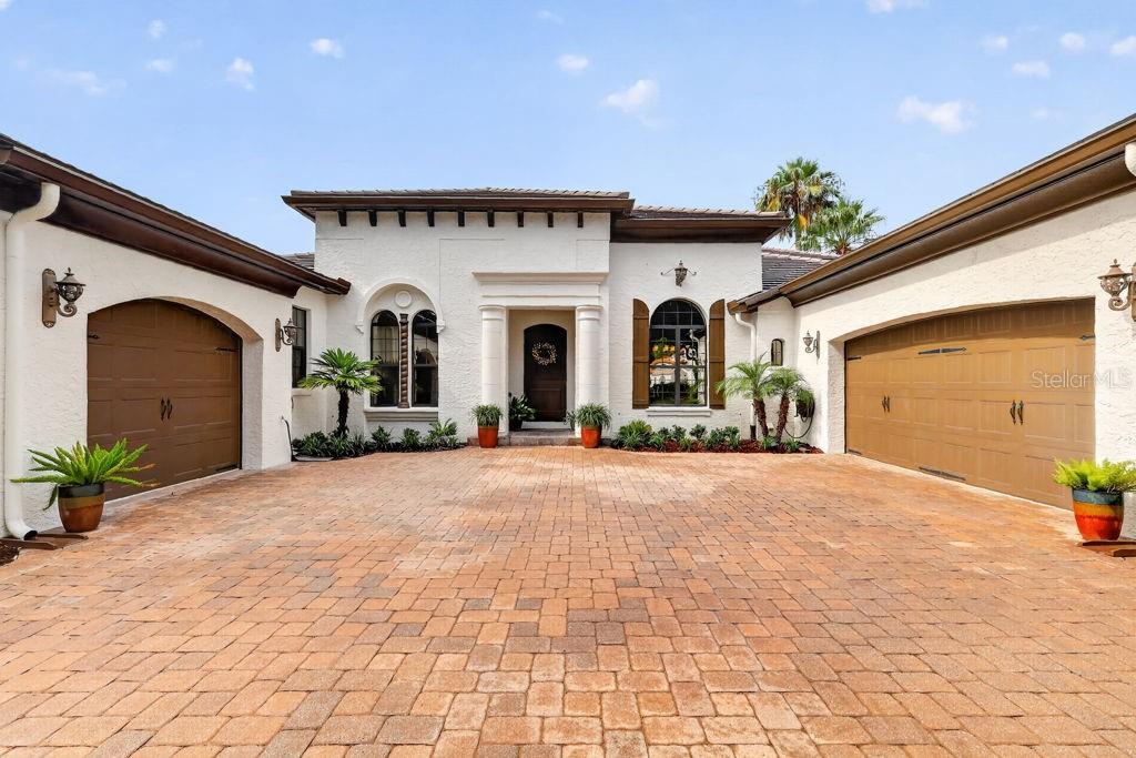 A white stucco house features a brick paver driveway, two garage doors, and a central entrance — 9620 SAN FERNANDO COURT, HOWEY IN THE HILLS, FL