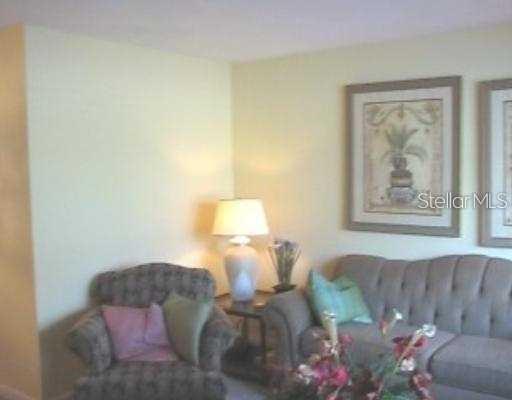 A living room features a patterned armchair, a sofa with teal pillows, and a table lamp — 1345 DREW STREET UNIT 5, CLEARWATER, FL