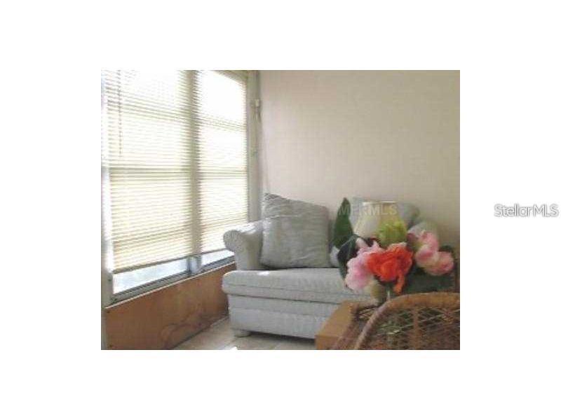 A light-colored armchair sits next to a window with closed blinds in a small room — 1345 DREW STREET UNIT 5, CLEARWATER, FL