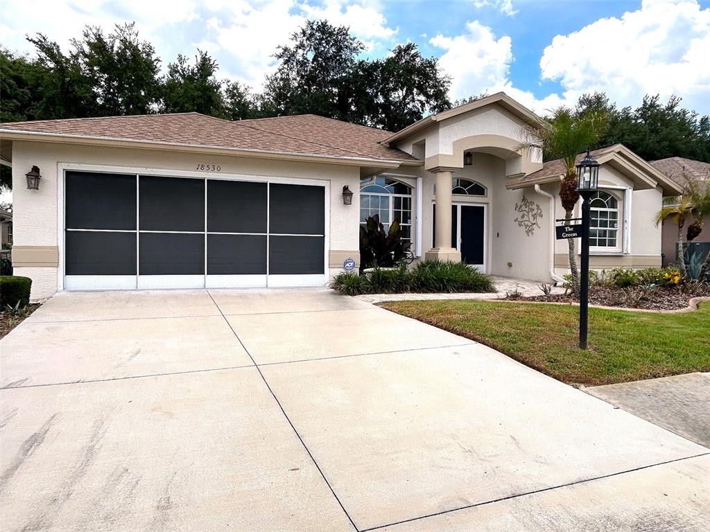 A single-story house with a beige stucco exterior, a screened garage, and a concrete driveway — 18530 WATER LILY LANE, HUDSON, FL