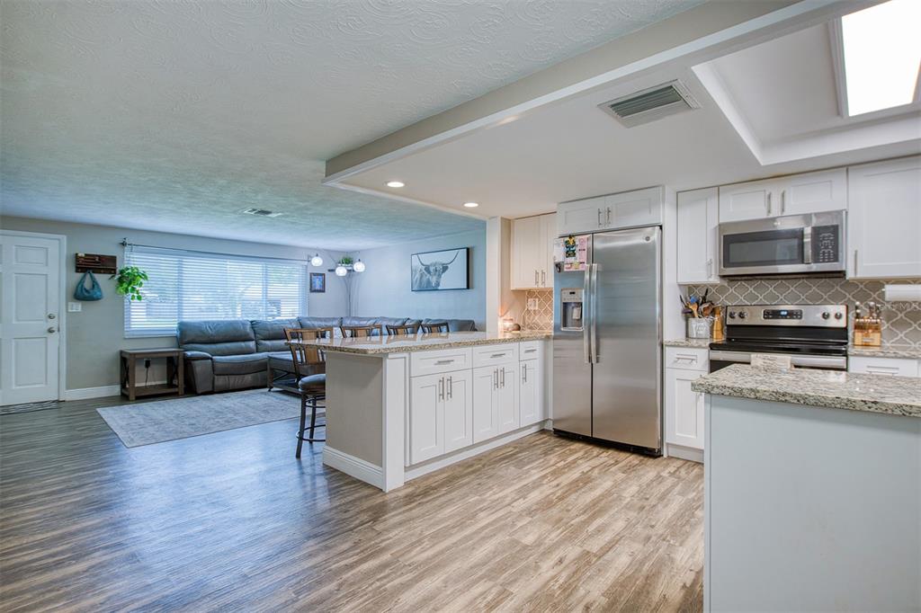 An open-concept kitchen with white cabinets and granite countertops overlooks a living room area — 1440 WISCONSIN AVENUE, PALM HARBOR, FL