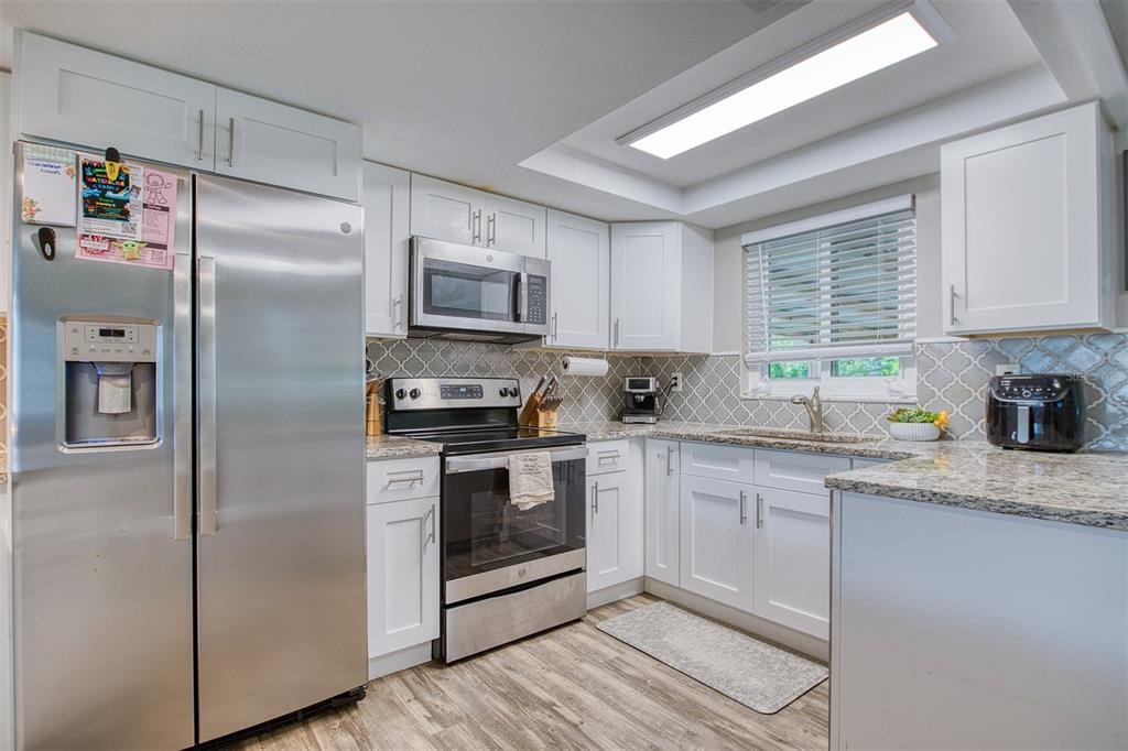 A kitchen with white cabinets, stainless steel appliances, granite countertops, and a gray tile backsplash — 1440 WISCONSIN AVENUE, PALM HARBOR, FL