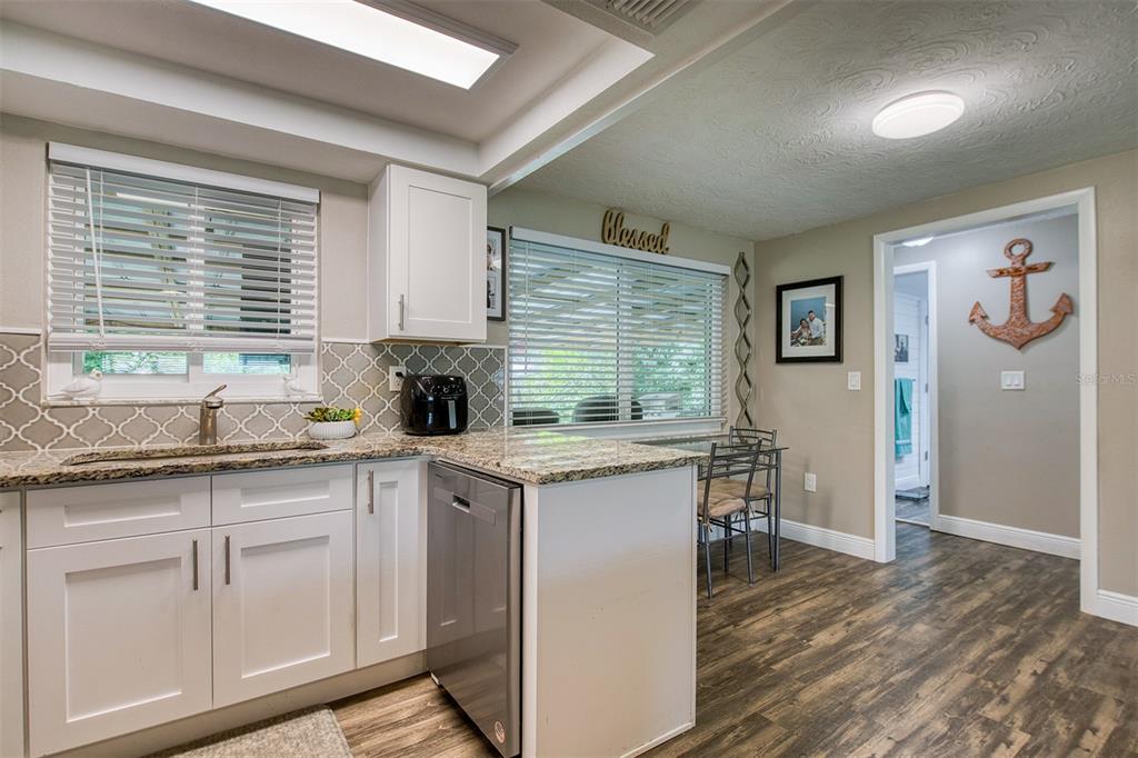 A kitchen features white cabinets, granite countertops, a stainless steel dishwasher, and wood-look flooring — 1440 WISCONSIN AVENUE, PALM HARBOR, FL