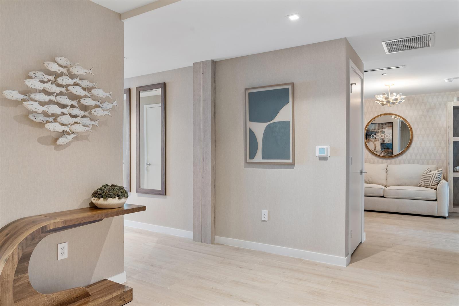 A hallway features light wood flooring, a sculptural wooden console table, and wall-mounted art — 1116 N Ocean Boulevard # 304, Pompano Beach FL 33062, POMPANO BEACH, FL