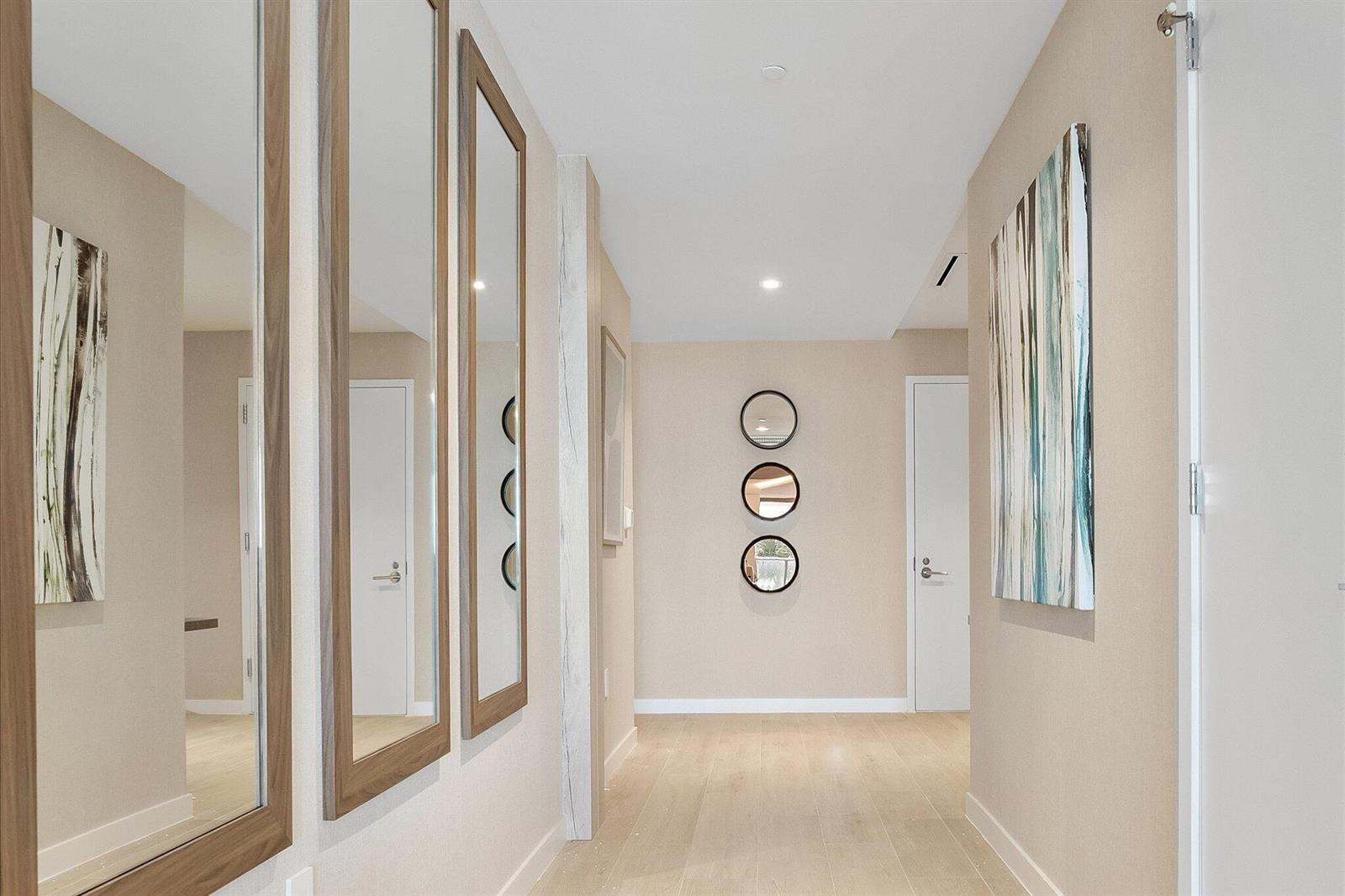 A hallway with light wood floors, beige walls, vertical mirrors, and circular wall decor — 1116 N Ocean Boulevard # 304, Pompano Beach FL 33062, POMPANO BEACH, FL