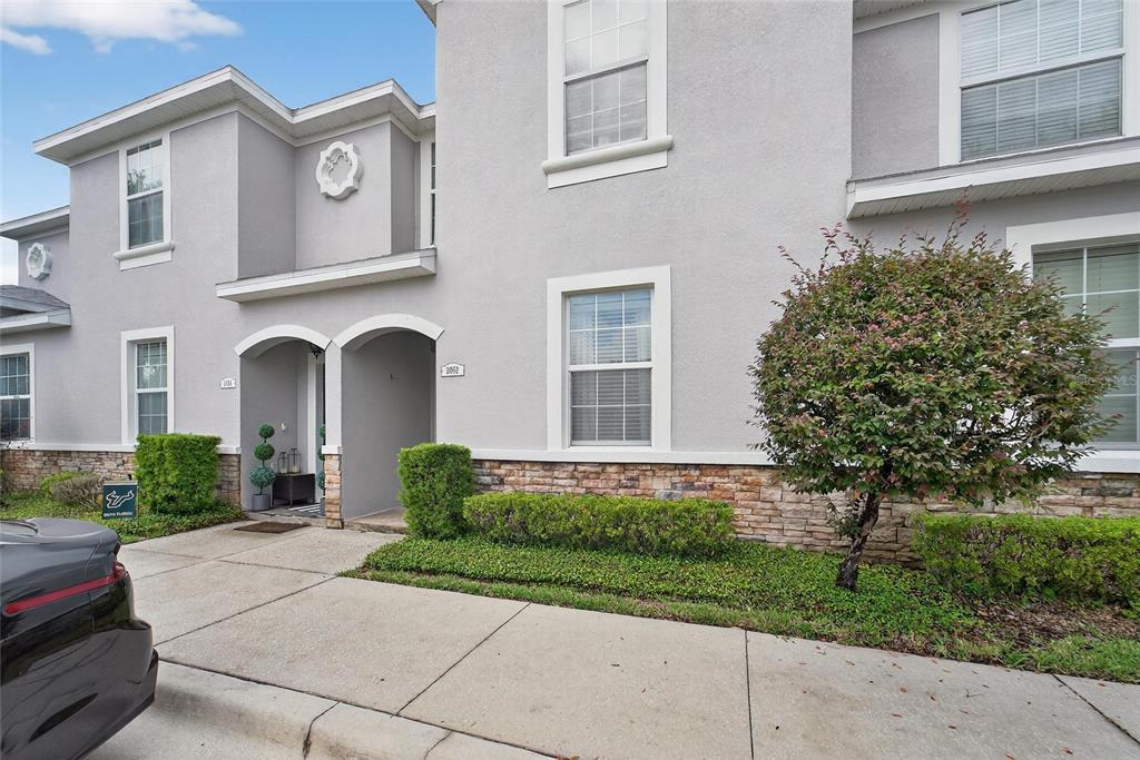 A two-story townhouse exterior features gray stucco walls, stone accents, and a concrete driveway — 2052 GREENWOOD VALLEY DRIVE, PLANT CITY, FL