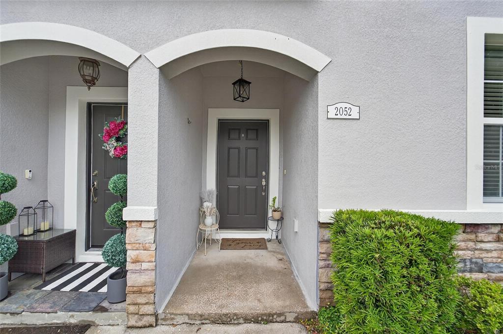 A gray front door is centered in a covered entryway with stone accents and landscaping — 2052 GREENWOOD VALLEY DRIVE, PLANT CITY, FL
