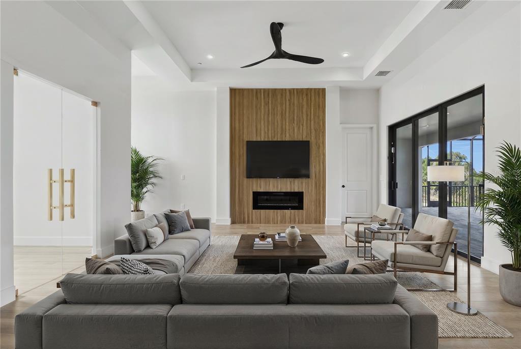 A modern living room features a wood-paneled fireplace wall, gray sectional sofa, and sliding doors — 14192 FORT MYERS AVENUE, PORT CHARLOTTE, FL