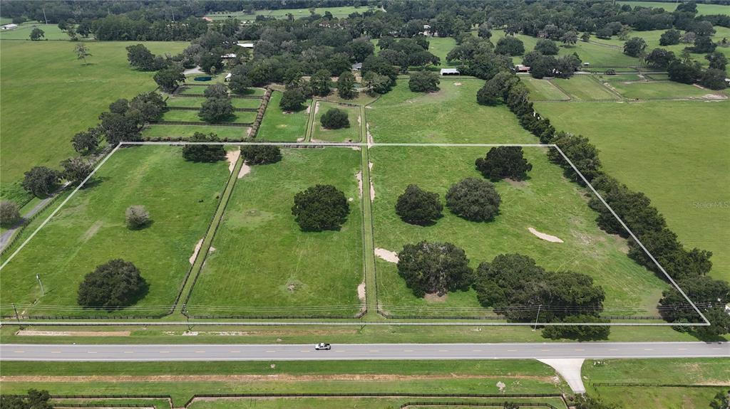 An aerial view shows a large, fenced grassy pasture with scattered trees along a road — 13460 NW GAINESVILLE ROAD, REDDICK, FL