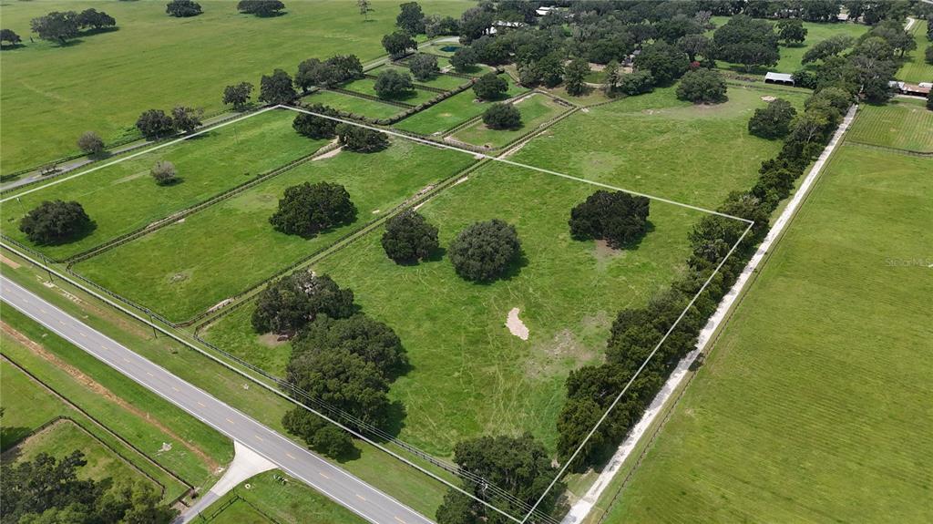 An aerial view shows a large, fenced grassy pasture with scattered trees along a road — 13460 NW GAINESVILLE ROAD, REDDICK, FL
