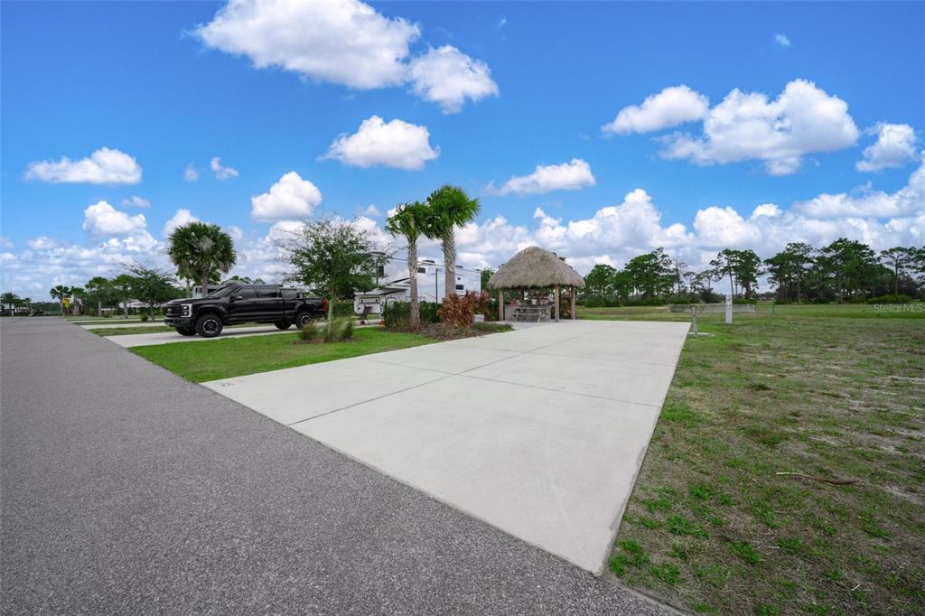 A concrete RV pad features a tiki hut and palm trees under a blue sky — HIGHWAY 630 E UNIT 15, LAKE WALES, FL