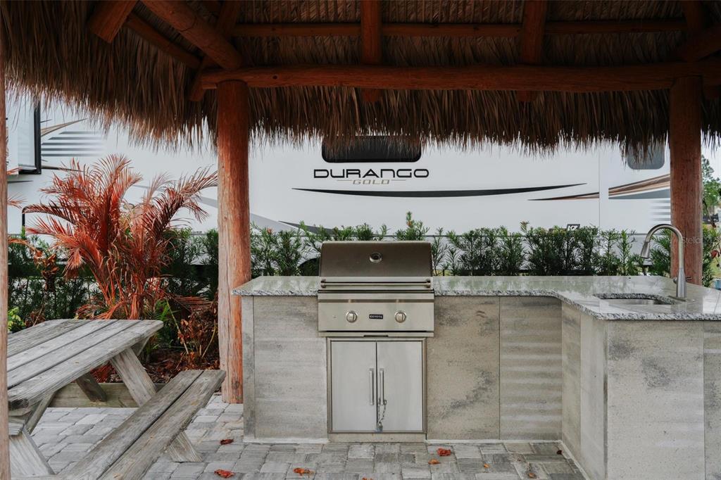 An outdoor kitchen with a stainless steel grill and sink sits under a thatched roof — HIGHWAY 630 E UNIT 15, LAKE WALES, FL