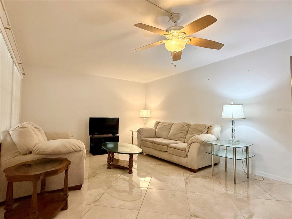 A living room features light-colored tile floors, a ceiling fan, and beige upholstered furniture — 4455 DUHME ROAD UNIT 203, ST PETERSBURG, FL