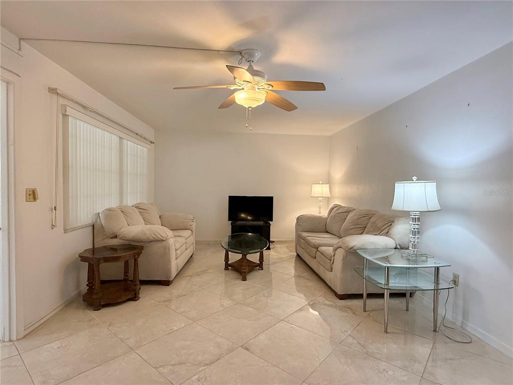 A living room features light-colored tile flooring, two sofas, a glass coffee table, and a ceiling fan — 4455 DUHME ROAD UNIT 203, ST PETERSBURG, FL