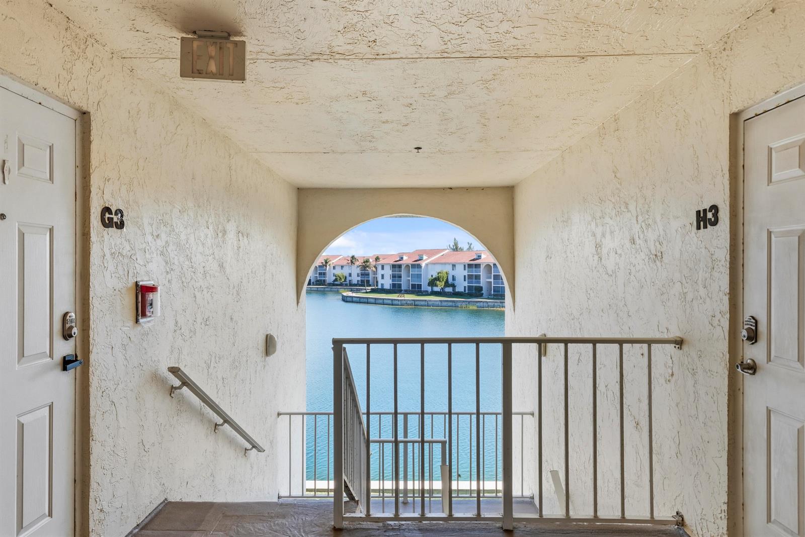 An outdoor apartment hallway features two unit doors, a staircase, and a view of water — 4452 NE Ocean Boulevard # C3, Jensen Beach FL 34957, JENSEN BEACH, FL
