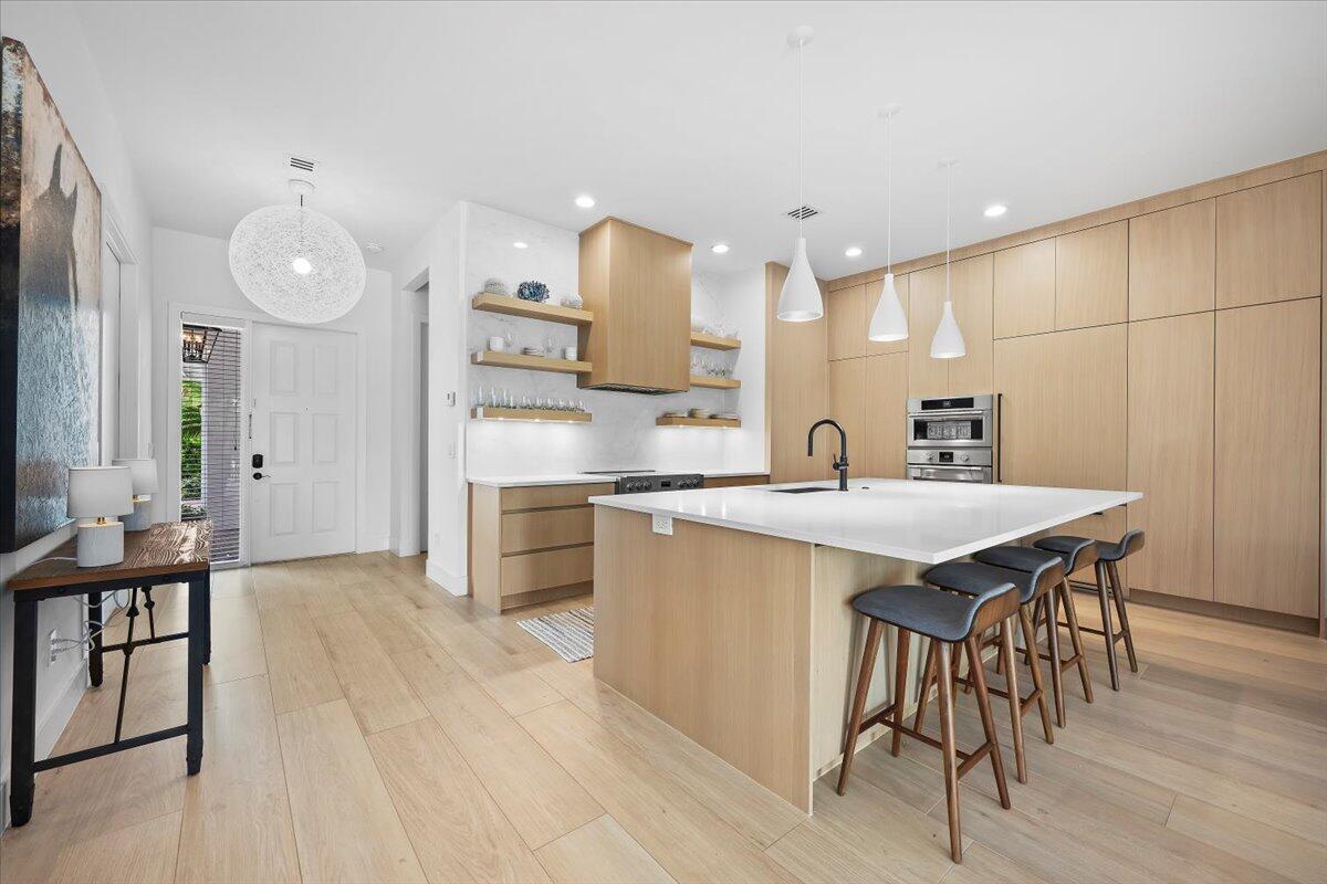 A modern kitchen features light wood cabinetry, a white island with bar seating, and pendant lighting — 2951 Twin Oaks Way, Wellington FL 33414, WELLINGTON, FL