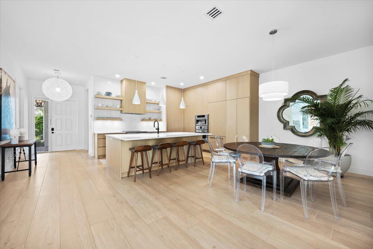 A modern kitchen and dining area feature light wood cabinetry, a large island, and chairs — 2951 Twin Oaks Way, Wellington FL 33414, WELLINGTON, FL