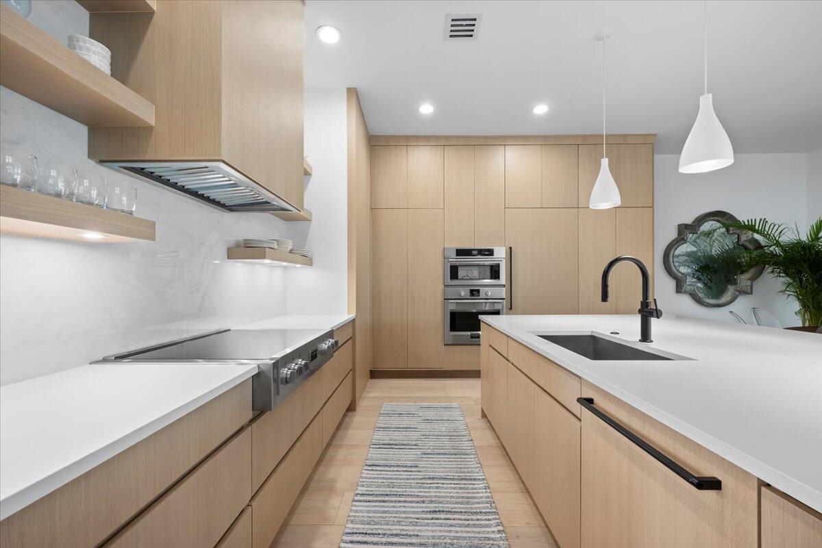 A modern kitchen features light wood cabinetry, white countertops, a central island, and stainless steel appliances — 2951 Twin Oaks Way, Wellington FL 33414, WELLINGTON, FL