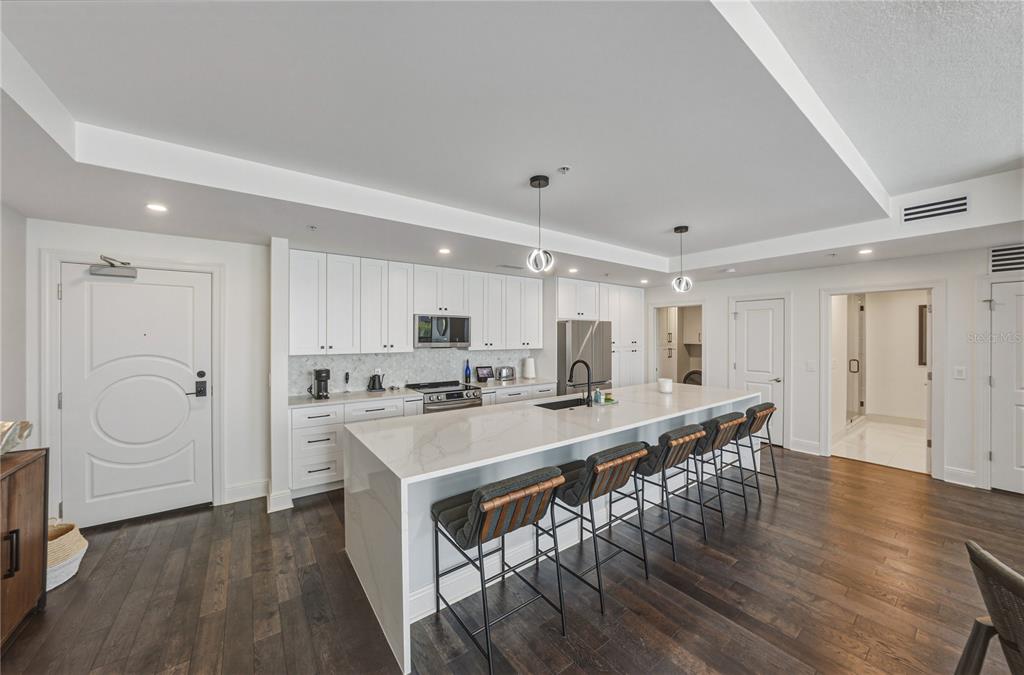 A modern kitchen features white cabinetry, a large quartz island with bar seating, and hardwood floors — 1227 E MADISON STREET UNIT 504, TAMPA, FL