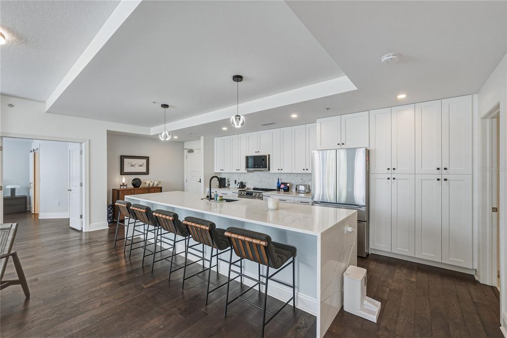 A modern kitchen features white cabinetry, a large marble-topped island, and dark wood flooring — 1227 E MADISON STREET UNIT 504, TAMPA, FL