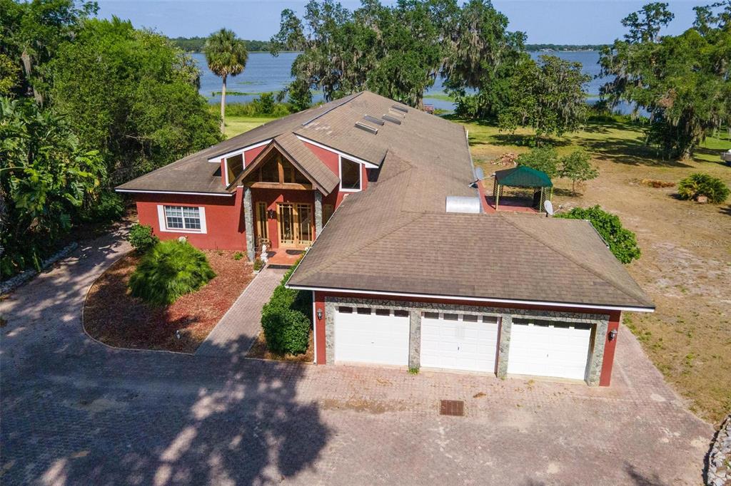 An aerial view of a red house with a three-car garage and a lakefront backyard — 2400 N GRIFFIN DRIVE, LEESBURG, FL