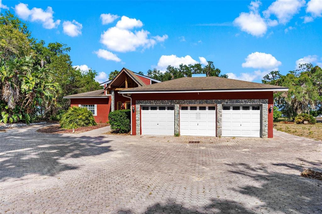 A red house with a three-car garage and a paved driveway under a blue sky — 2400 N GRIFFIN DRIVE, LEESBURG, FL