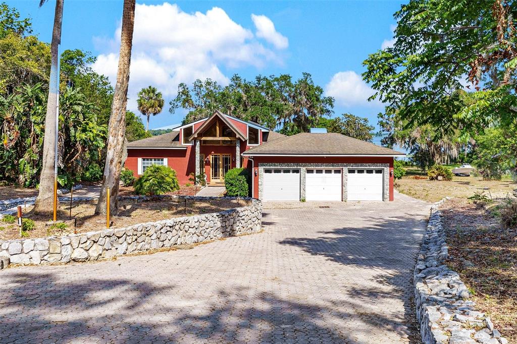 A red house with a three-car garage and a stone retaining wall along the driveway — 2400 N GRIFFIN DRIVE, LEESBURG, FL