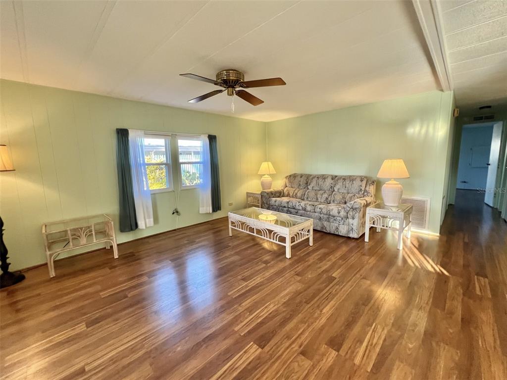 A living room features light green walls, wood-look flooring, a floral sofa, and a ceiling fan — 169 BOUGAINVILLEA DRIVE, LEESBURG, FL