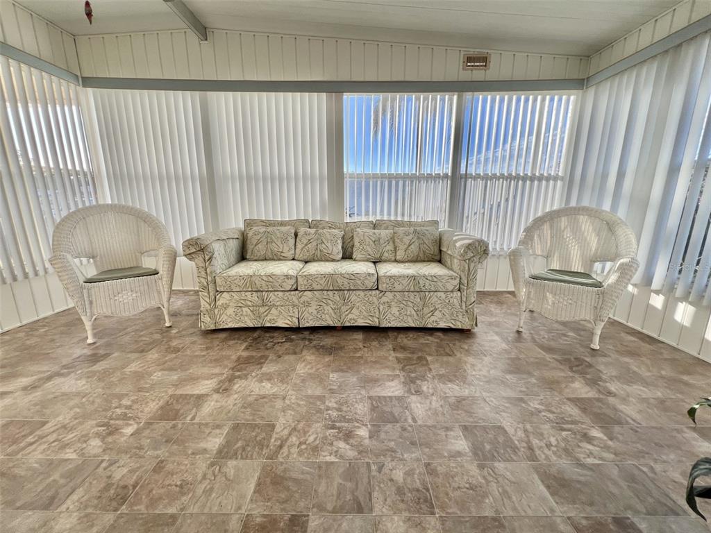 A sunroom features a floral sofa, two white wicker chairs, and brown tile flooring — 169 BOUGAINVILLEA DRIVE, LEESBURG, FL