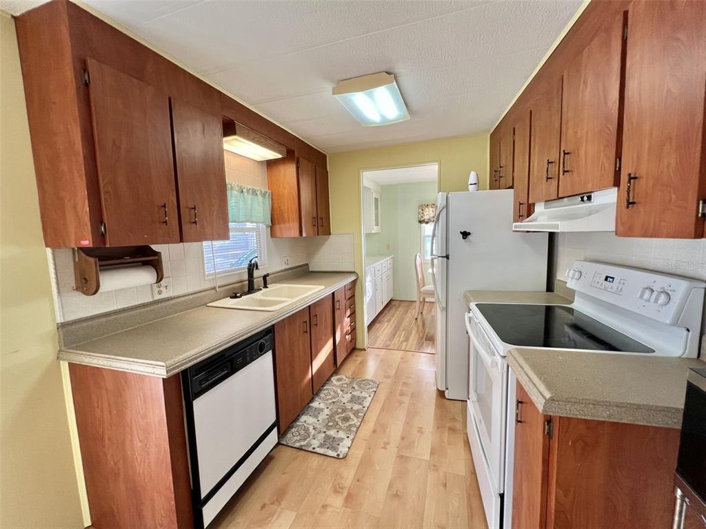 A kitchen with wood cabinets, white appliances, laminate countertops, and light wood-look flooring — 169 BOUGAINVILLEA DRIVE, LEESBURG, FL