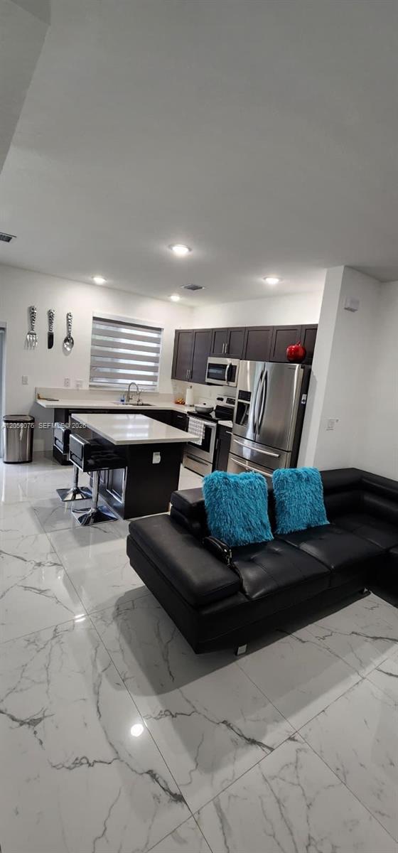 A modern kitchen with dark cabinetry and a white island sits beside a black sofa — 1664 SE 27th Ter, Homestead FL 33035, HOMESTEAD, FL