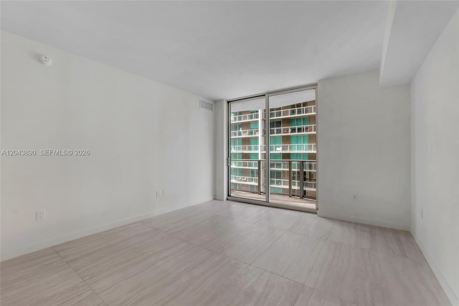 An empty room with light-colored tile flooring and a sliding glass door leading to a balcony — 77 SE 5th Street # 1708, Miami FL 33131, MIAMI, FL