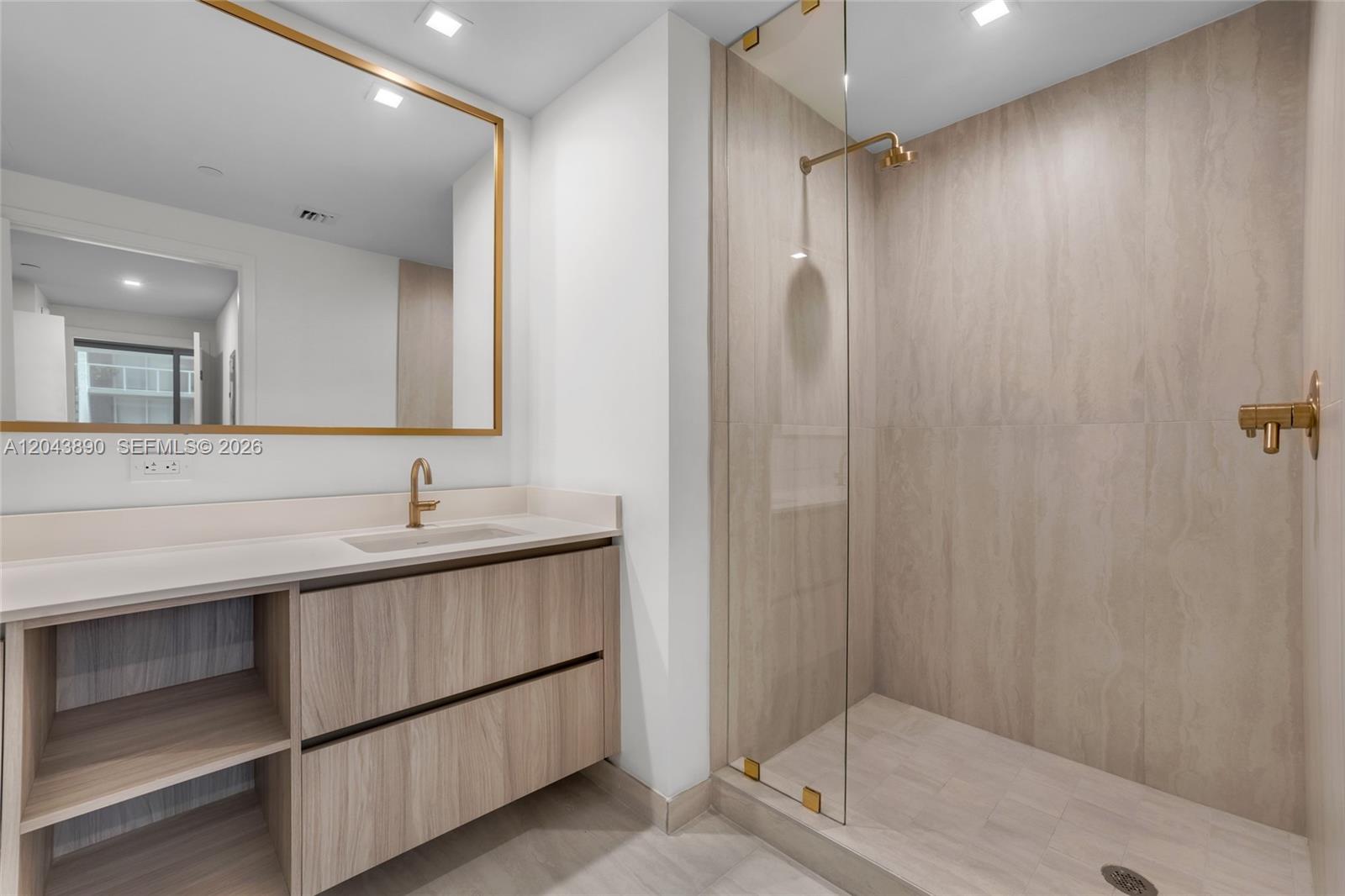 A modern bathroom features a wood-toned vanity, a gold-framed mirror, and a glass-enclosed walk-in shower — 77 SE 5th Street # 1708, Miami FL 33131, MIAMI, FL