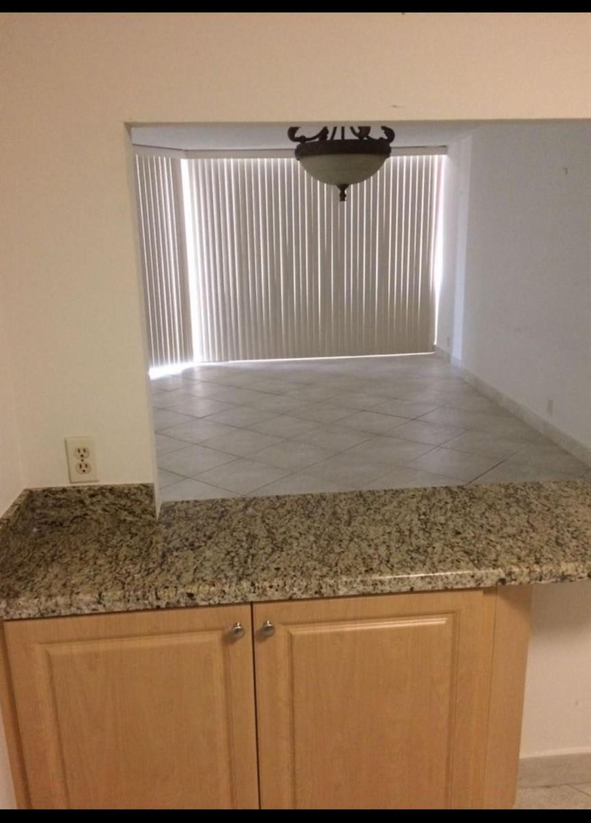 A kitchen pass-through window overlooks a dining area with tile floors and vertical blinds — 1865 Brickell Avenue # A707, Miami FL 33129, MIAMI, FL