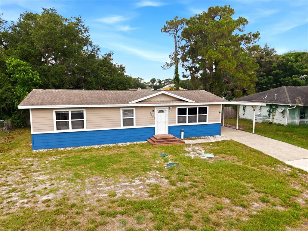 A backyard view of a single-story house with a screened-in porch and large oak trees — 6592 EMIL AVENUE, COCOA, FL
