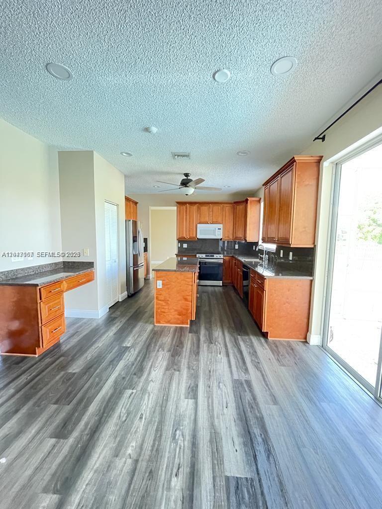 A kitchen features wood cabinets, dark countertops, a center island, and gray wood-look flooring — 558 Stonemont Dr # 558, Weston FL 33326, WESTON, FL