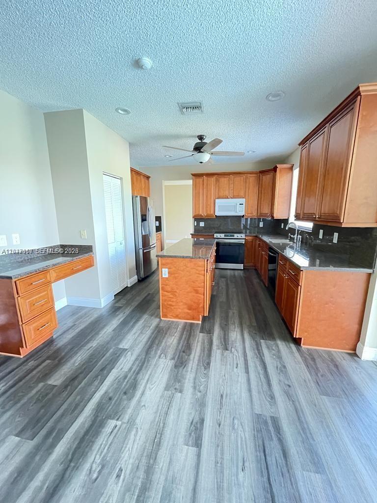A kitchen features wood cabinets, granite countertops, a center island, and gray wood-look flooring — 558 Stonemont Dr # 558, Weston FL 33326, WESTON, FL