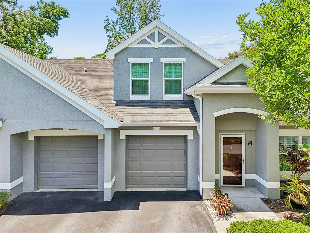 A two-story house exterior features two garage doors, a front entrance, and gray stucco siding — 3638 TRAFALGAR WAY UNIT 102, PALM HARBOR, FL