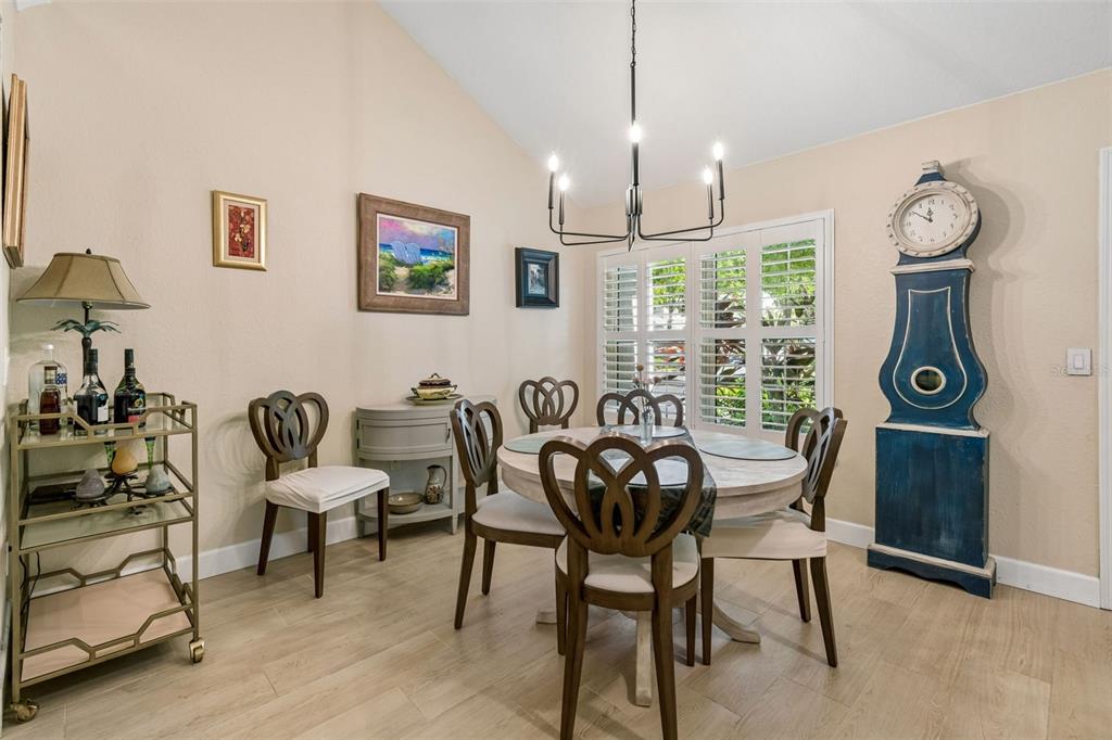 A dining room features a round table, chairs, a bar cart, and a tall grandfather clock — 3638 TRAFALGAR WAY UNIT 102, PALM HARBOR, FL