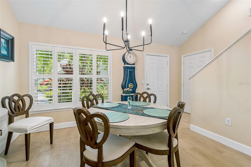 A dining room features a round table, four chairs, a blue grandfather clock, and shutters — 3638 TRAFALGAR WAY UNIT 102, PALM HARBOR, FL