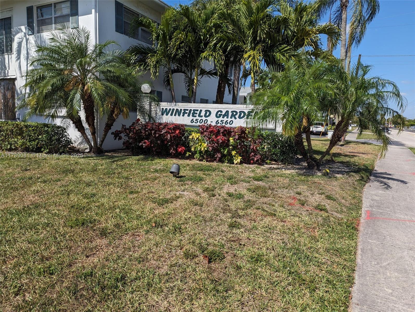 A white apartment building sign stands behind palm trees and shrubs on a grassy lawn — 6510 Winfield Blvd # 103, Margate FL 33063, MARGATE, FL