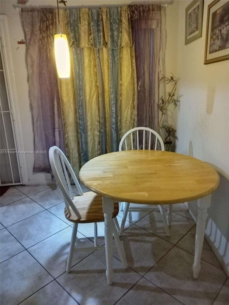 A dining area features a round wooden table with two white chairs on tiled flooring — 6510 Winfield Blvd # 103, Margate FL 33063, MARGATE, FL