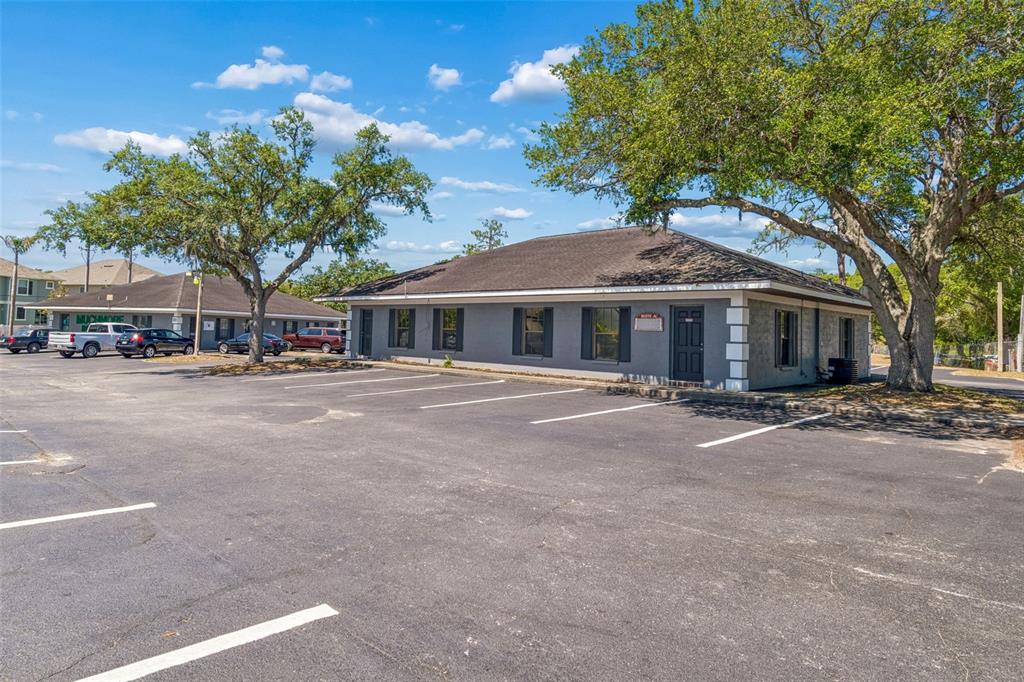 A gray, single-story commercial building with a parking lot and large trees in front — 7517 LITTLE ROAD, NEW PORT RICHEY, FL