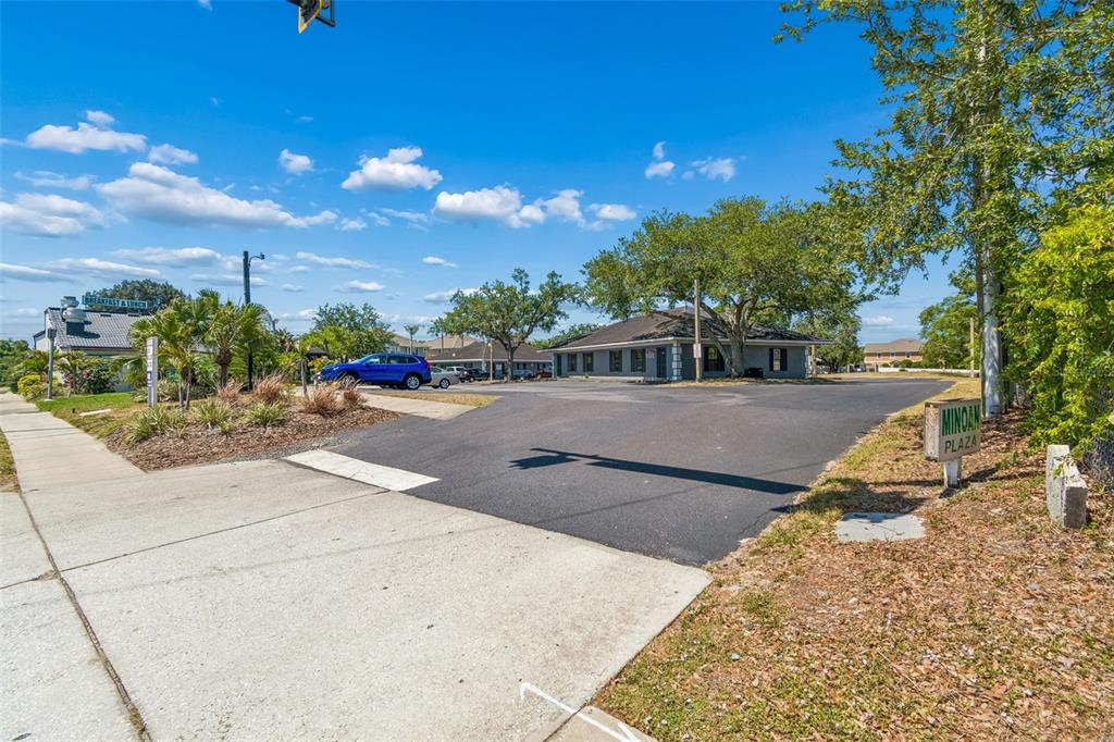 A paved driveway leads to a gray commercial building with a sign reading Minoan Plaza — 7517 LITTLE ROAD, NEW PORT RICHEY, FL